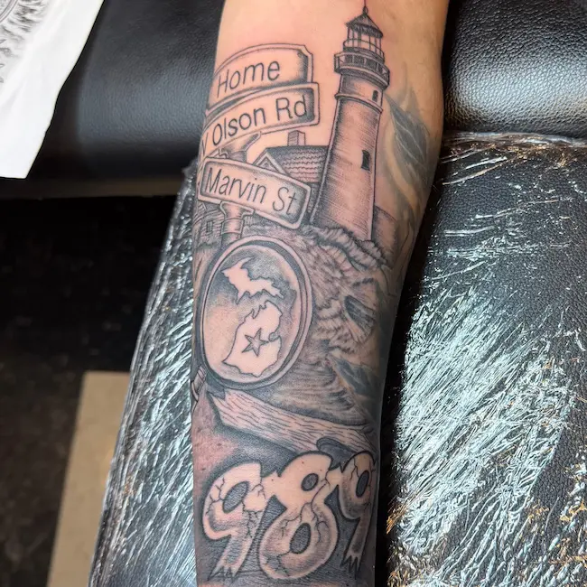 Black and grey forearm tattoo sleeve of beach, lighthouse, street signs, zip code, and other Michigan artifacts.